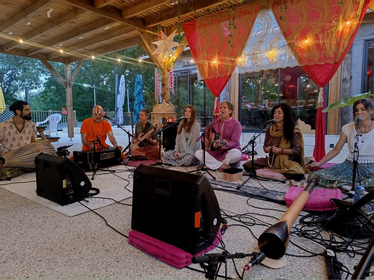 Soirée kirtan à la Maison pour Tous : chanteurs, harmonium, guitare et mridanga assis sous la pergola, guirlandes lumineuses